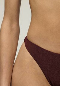 Burgundy bikini alsó, amely magas kivágású dizájnnal, sima textúrával és minimális takarással rendelkezik, kiemelve a letisztult vonalakat és a diszkrét varrási részleteket.