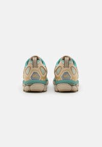 Scarpe sportive con una combinazione di colori beige e turchese, tomaia in rete, colletto imbottito e accento del logo sul tallone.