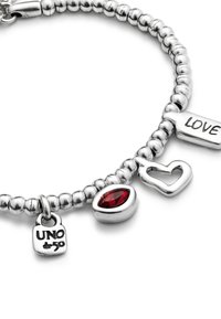 Bracelet en perles argentées avec trois breloques : une pierre précieuse rouge, une forme de cœur, et une plaque gravée avec "LOVE" et "UNO".