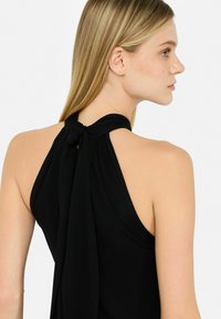 Zwarte haltertop met een geknoopte rugontwerp, gemaakt van een soepele stof, met een open rug en een lichte, vloeiende textuur.