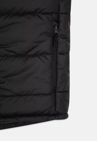 Černá zateplená vesta s prošívaným designem, vertikálními švy a boční kapsou na zip s černým kováním. Hladká texturovaná látka.