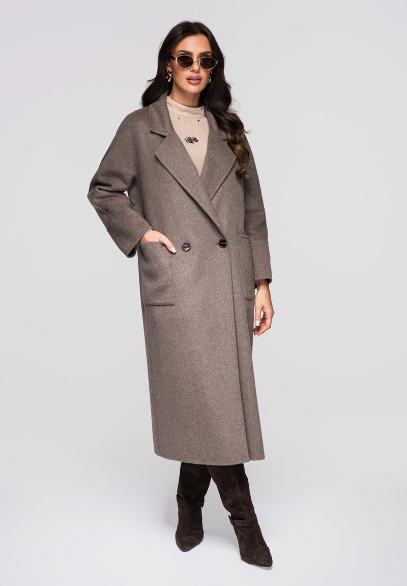 Manteau en laine croisé de couleur marron clair, avec de grandes poches et une coupe ample. Associé à un haut beige et des bottines marron foncé.