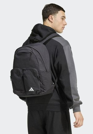 Black Adidas backpack with a grid pattern, multiple zippered pockets, padded shoulder straps, and a triangular logo at the bottom.