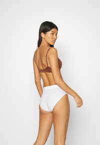 Bruine bh met verstelbare bandjes en een gouden sluiting, gecombineerd met witte onderbroek met hoge taille. Glad materiaal en aansluitend ontwerp.