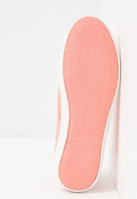 Semelle de basket rose avec caoutchouc texturé pour l'adhérence, bord blanc. Le design est minimaliste et lisse, présentant une forme simple et arrondie.