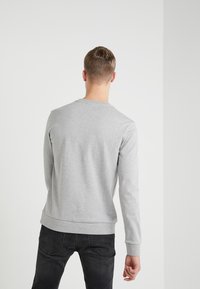 Grauer Kapuzenpullover mit langen Ärmeln, rundem Ausschnitt und gerippten Bündchen, kombiniert mit dunklen Jeans. Weicher Stoff mit glatter Textur.