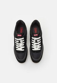 Schwarze Sneaker mit weißen Schnürsenkeln, aus einer Mischung von Wildleder und Stoffmaterialien, mit einer gepolsterten Zunge und einem roten Logo-Tag an jedem Schuh.
