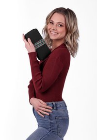 Black fabric clutch with colorful zigzag pattern. Rectangular shape with a zip closure, held by a model in a burgundy top and blue jeans.