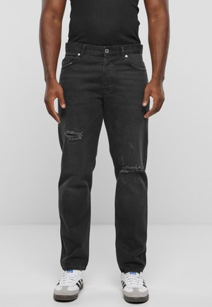 Zwarte denim jeans met een losse pasvorm, versleten details op de knieën en een klassieke vijf-pocketontwerp. Gecombineerd met witte sneakers.