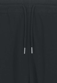 Gros plan sur un tissu noir avec des cordons de serrage noirs ornés d'embouts métalliques argentés aux extrémités.