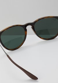 Zonnebril met een schildpadachtig frame, groene lenzen en een strak ontwerp, met een zilveren metalen scharnier en een donkerbruine poot.
