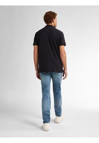 Černý polo tričko s krátkým rukávem, zkombinované se světle modrými vybledlými džíny a bílými teniskami. Design je jednoduchý a klasický.