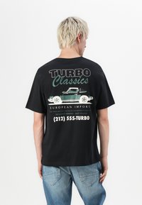Sort bomulds t-shirt med et grafisk print på ryggen, der viser en grøn bil, teksten "TURBO Classics" og kontaktoplysninger i hvid.
