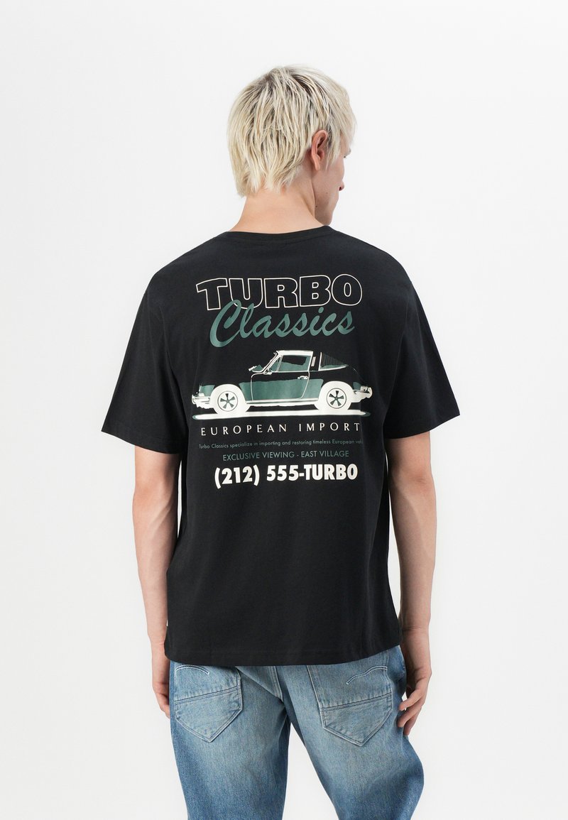 Sort bomulds t-shirt med et grafisk print på ryggen, der viser en grøn bil, teksten "TURBO Classics" og kontaktoplysninger i hvid.