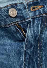 Denim jeans with a light blue wash, featuring a metal button, a zipper fly, and orange stitching along the seams and waistline.