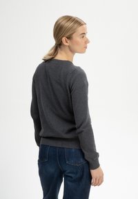Grau gestrickter Pullover mit rundem Halsausschnitt und gerippten Bündchen, kombiniert mit dunkelblauen Jeans. Der Stoff wirkt weich mit einer glatten Textur.