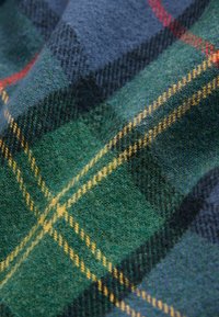 Tissu tissé présentant un motif à carreaux vert, bleu et jaune avec une texture douce et des fibres visibles, mettant en valeur la profondeur et le contraste des couleurs.