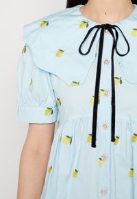 Jasnoniebieska sukienka z dużym kołnierzem, haftem w kształcie cytryny, bufkami oraz czarną tasiemką, z perłowymi guzikami z przodu.