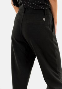Pantalons noirs en tissu texturé, dotés d'une taille haute, de poches arrière, et d'un petit logo au dos.