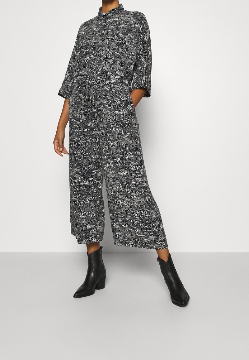 Svartvitt mönstrad jumpsuit med krage, korta ärmar, vida ben och sidofickor, matchad med svarta ankelstövlar.