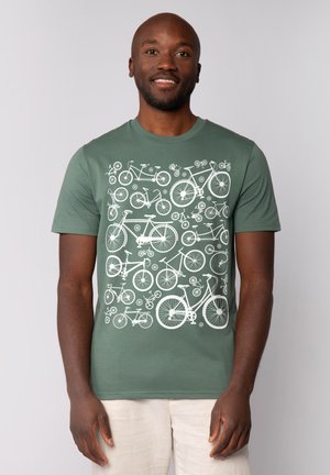 Groene katoenen t-shirt met een wit fietsontwerp, inclusief verschillende stijlen en maten fietsen in een herhaald patroon.