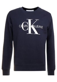Mörkblå sweatshirt i bomull med rund halsringning, ribbade muddar och en stor vit logotyptext "CALVIN KLEIN JEANS" på framsidan.