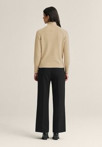 Beige kaulusneule, jossa on raglan-hihat, yhdistettynä korkeavyötäröisiin, leveälahkeisiin mustiin housuihin ja mustiin korkeaosan nilkkasaappaisiin.