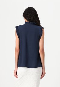 Blusa senza maniche blu navy con dettagli a volant lungo le spalle, realizzata in un tessuto morbido con una vestibilità rilassata e un orlo arrotondato.