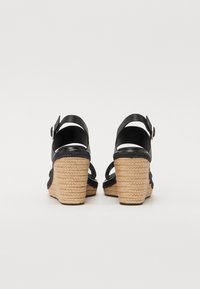 Sandalias de cuña de cuero negro con tacón de yute trenzado. Presenta una correa en el tobillo ajustable y un diseño de espalda abierta. Suela texturizada para un mejor agarre.