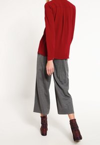 Chemise rouge à manches longues avec un dos boutonné, associée à un pantalon gris à jambes larges. Bottines texturées avec un motif coloré.
