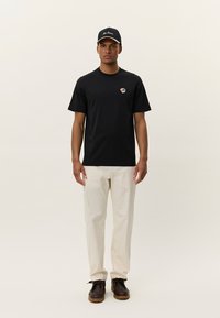 Black cotton t-shirt with a rose graphic on the chest, paired with cream-colored pants and a navy cap featuring white embroidery. Brown shoes.