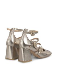 Scarpe con tacco alto metalliche dorate, con punta appuntita, tacco a blocco spesso e tre decorazioni floreali con pietre trasparenti sui cinturini alla caviglia.