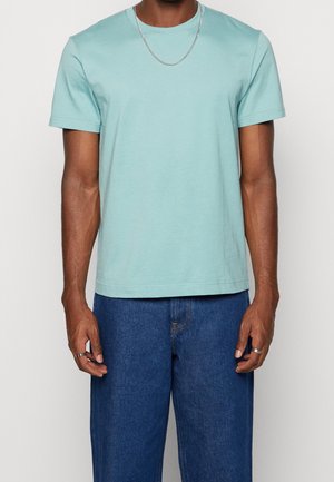 Jasnoniebieska bawełniana koszulka z okrągłym dekoltem i krótkimi rękawami, zestawiona z ciemnymi dżinsami. Prosty design, miękka tekstura.