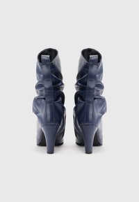 Boots din piele bleumarin, cu gât, cu un design relaxat, prevăzute cu toc înalt și un sistem de prindere pe spate pentru a fi ușor de încălțat. Textură netedă și strălucire subtilă.