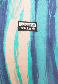 Barevná tkanina Adidas s abstraktními aqua a broskvovými pruhy, s černou etiketou, která ukazuje název značky a logo.