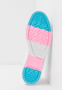 Suela de zapatilla blanca que presenta un patrón de goma segmentado en azul, rosa y blanco, con agarre texturizado, logotipo de marca en relieve y detalles en forma de diamante.