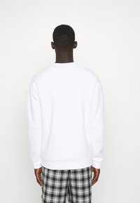 Vit crewneck-tröja med långa ärmar, mjuk textur och ribbade muddar, tillsammans med svarta och vita rutiga byxor.