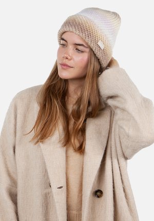 Knit beanie in gradient beige and cream, featuring a folded cuff and small logo tag. Worn with a beige wool blend coat and sweater.