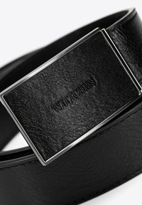 Cintura in pelle nera con una superficie liscia, caratterizzata da una fibbia rettangolare in argento con logo stampato e un design classico.