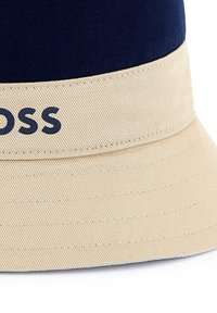Cappello a secchi navy con visiera beige. Presenta una cucitura decorativa e la parola "GROSS" in blu navy sulla sezione beige. Materiale in cotone.