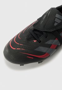 Svart fotballsko med røde og grå detaljer, med en teksturert overflate, lisser og et fremtredende "HYBRIDFEEL"-merke på siden.