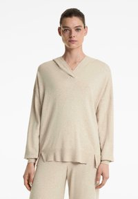 Beige, hosszú ujjú, kapucnis pulóver V-nyakkivágással. Puha, texturált anyag; lazán illeszkedő fazon, oldalsó hasítékokkal az alján.