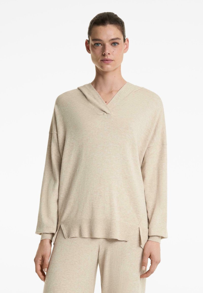 Beige, hosszú ujjú, kapucnis pulóver V-nyakkivágással. Puha, texturált anyag; lazán illeszkedő fazon, oldalsó hasítékokkal az alján.