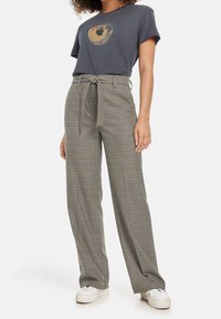 T-shirt gris avec un design graphique et un pantalon à jambes larges en carreaux avec un nœud à la taille. Le tissu semble lisse ; le pantalon a un motif à carreaux.