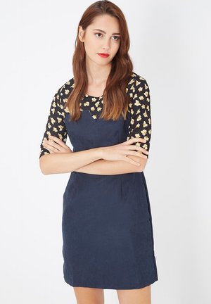 Vestido de ante azul marino con un diseño ajustado, que presenta un top negro con un patrón floral y mangas de tres cuartos. Materiales texturizados y suaves.