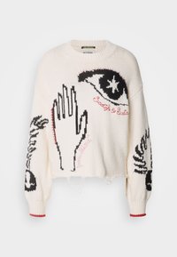 Pull couleur crème à coupe ample, orné de motifs noirs représentant un œil et une main, avec des détails de texte roses. Manches côtelées avec des accents rouges.