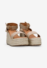 Sandales à plateau beiges avec une semelle en corde de jute, dotées d'une large bande au niveau des orteils et d'une sangle de cheville avec une boucle dorée. Texture lisse et design classique.