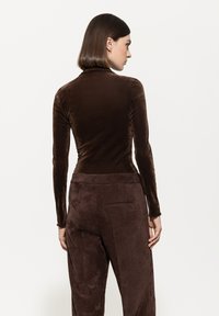 Brown velvet long-sleeve top with a high neck, paired with corduroy brown pants featuring textured stripes and side pockets.