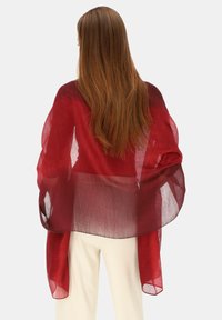 Czerwony przezroczysty szal z płynnym wzorem, lekką fakturą i nieco ciemniejszym obrzeżem, spływający na ramiona osoby.