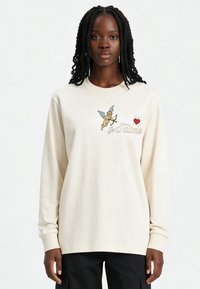 Sweat-shirt en coton crème à manches longues, arborant un graphique coloré de cupidon et le texte "je t’aime" orné sur le devant. Coupe décontractée.
